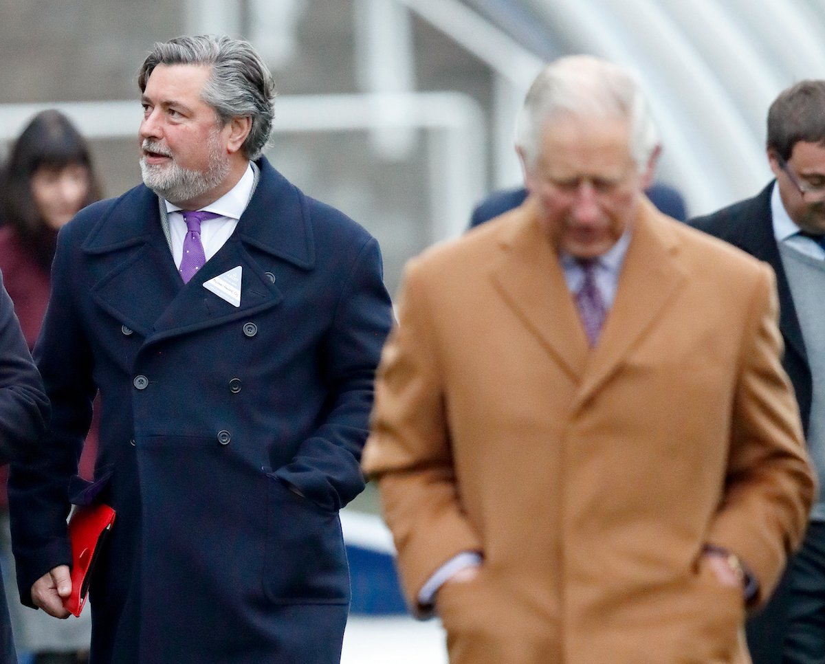 Michael Fawcett walks behind Prince Charles wearing a blue coat at The Prince's Countryside Fund Raceday