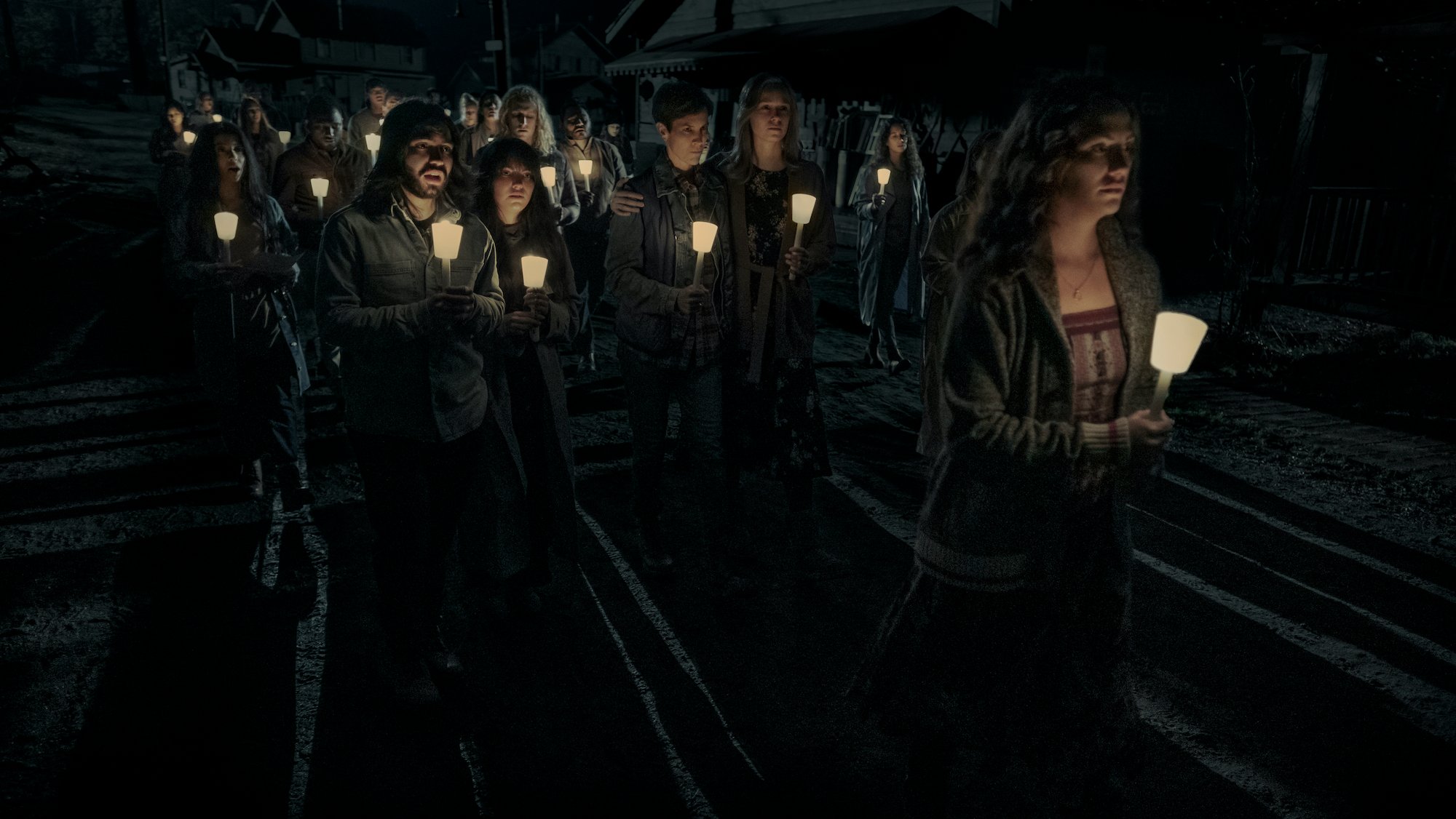 Cast members in a scene from 'Midnight Mass' holding candles while walking as a group