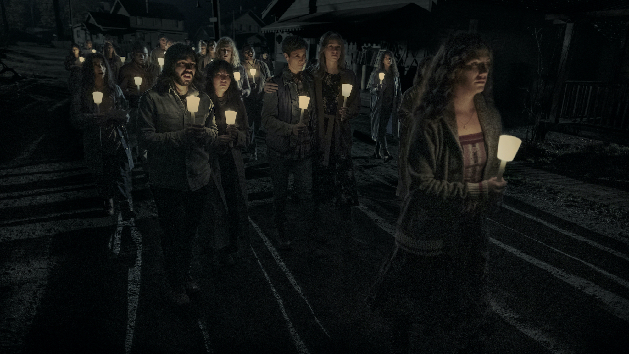 Cast members in a scene from 'Midnight Mass' holding candles while walking as a group