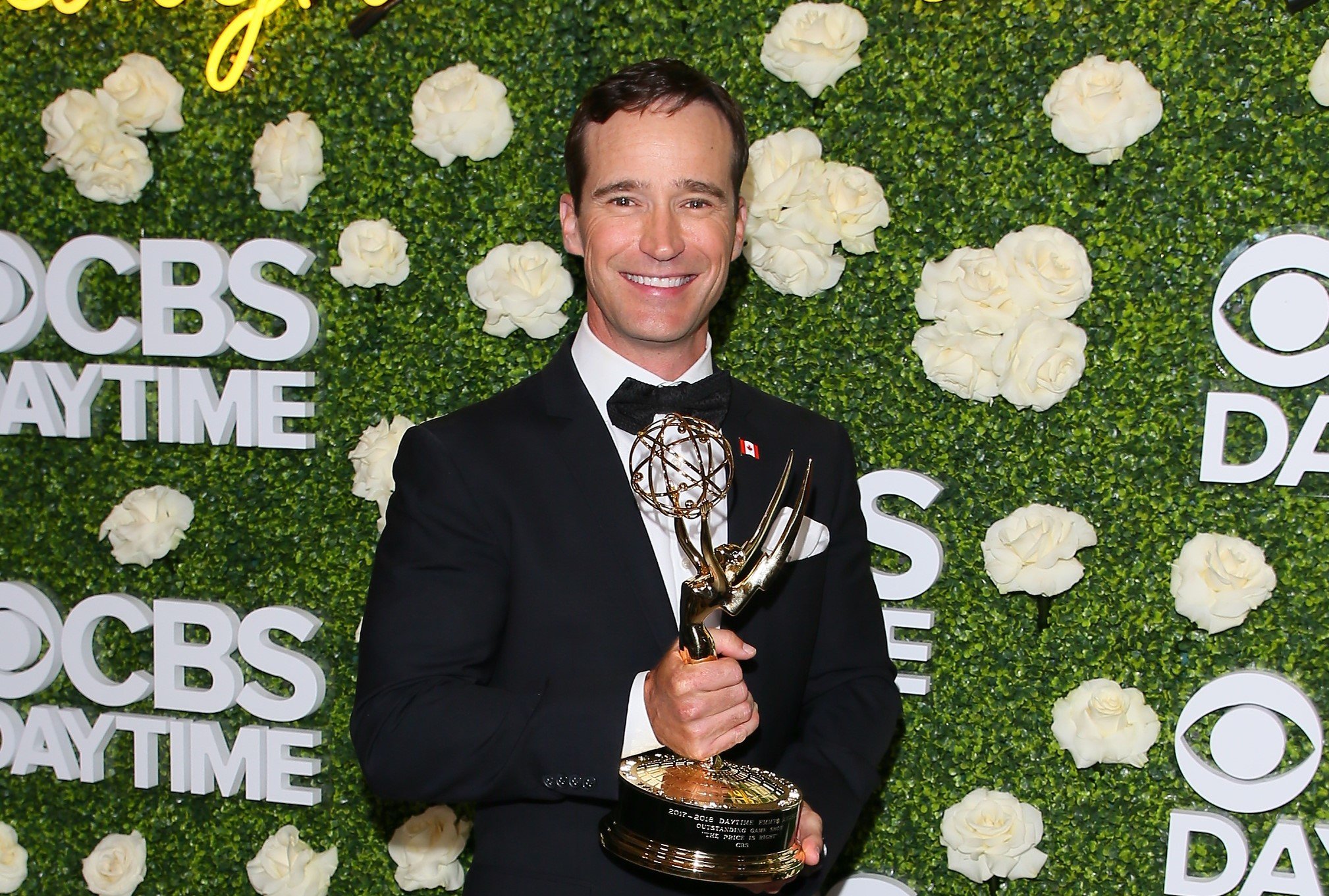 Mike Richards wears a tuxedo and holds a Daytime Emmy Award.