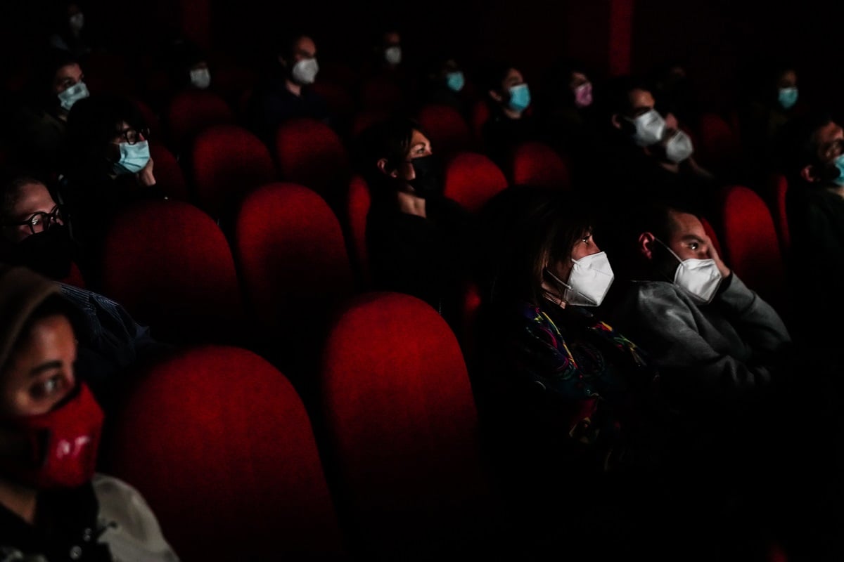 People wearing masks look at a screen in a movie theater. 