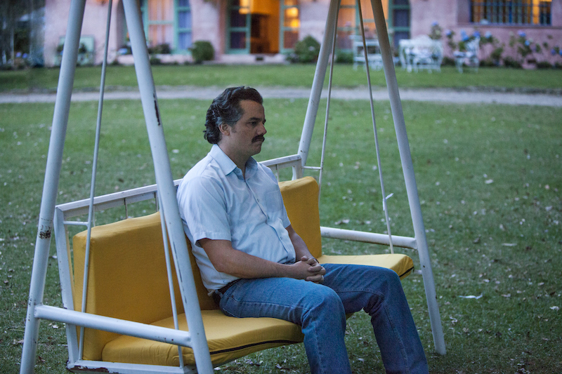 Wagner Moura as Pablo Escobar sits on a swing outside looking sad.