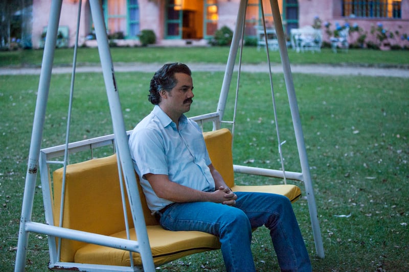 Wagner Moura as Pablo Escobar sits on a swing outside looking sad.