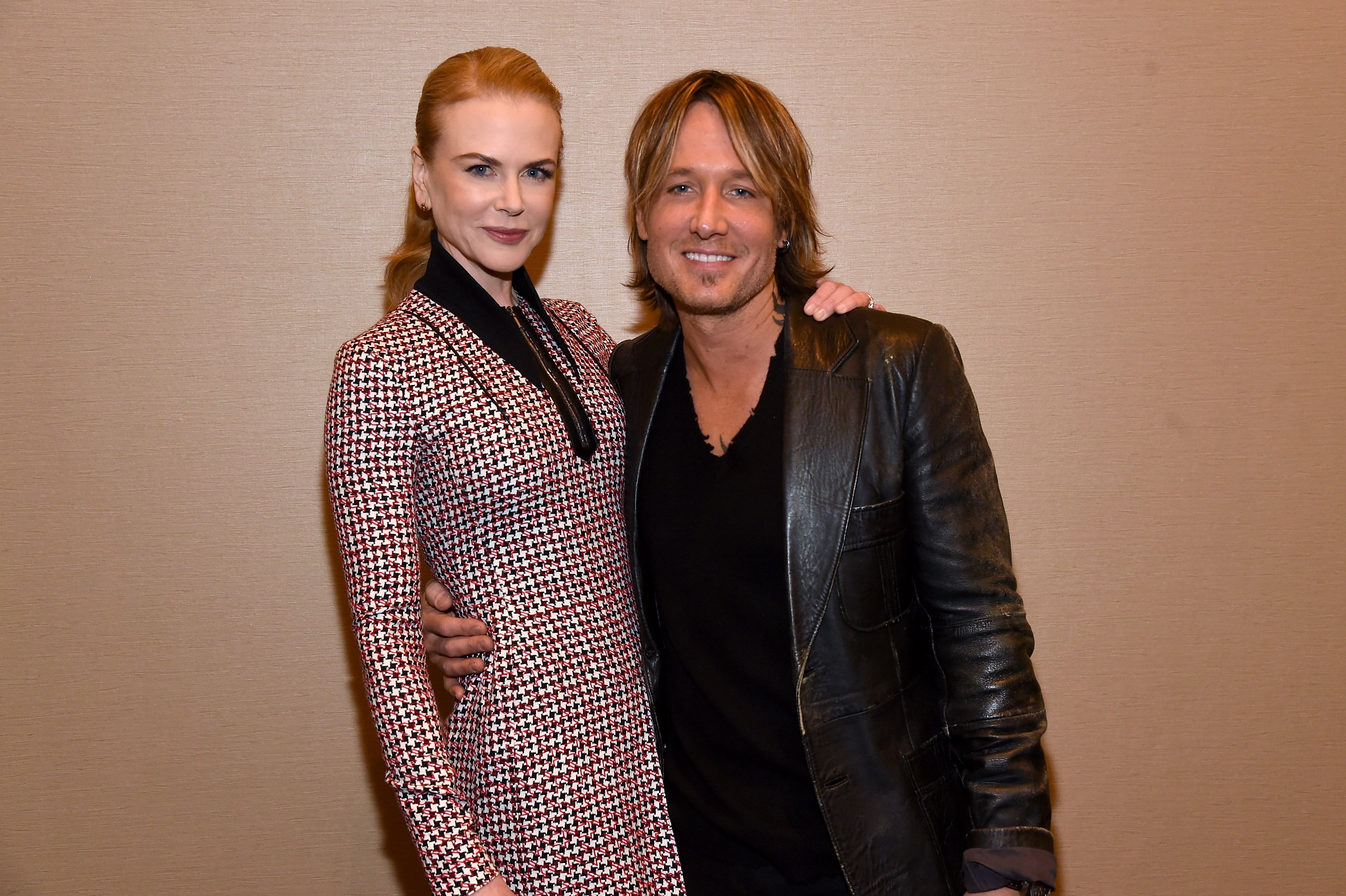 Nicole Kidman and Keith Urban smile for a photo. Kidman wears a long-sleeved patterned dress, and Urban wears a black v-neck shirt and leather jacket. 