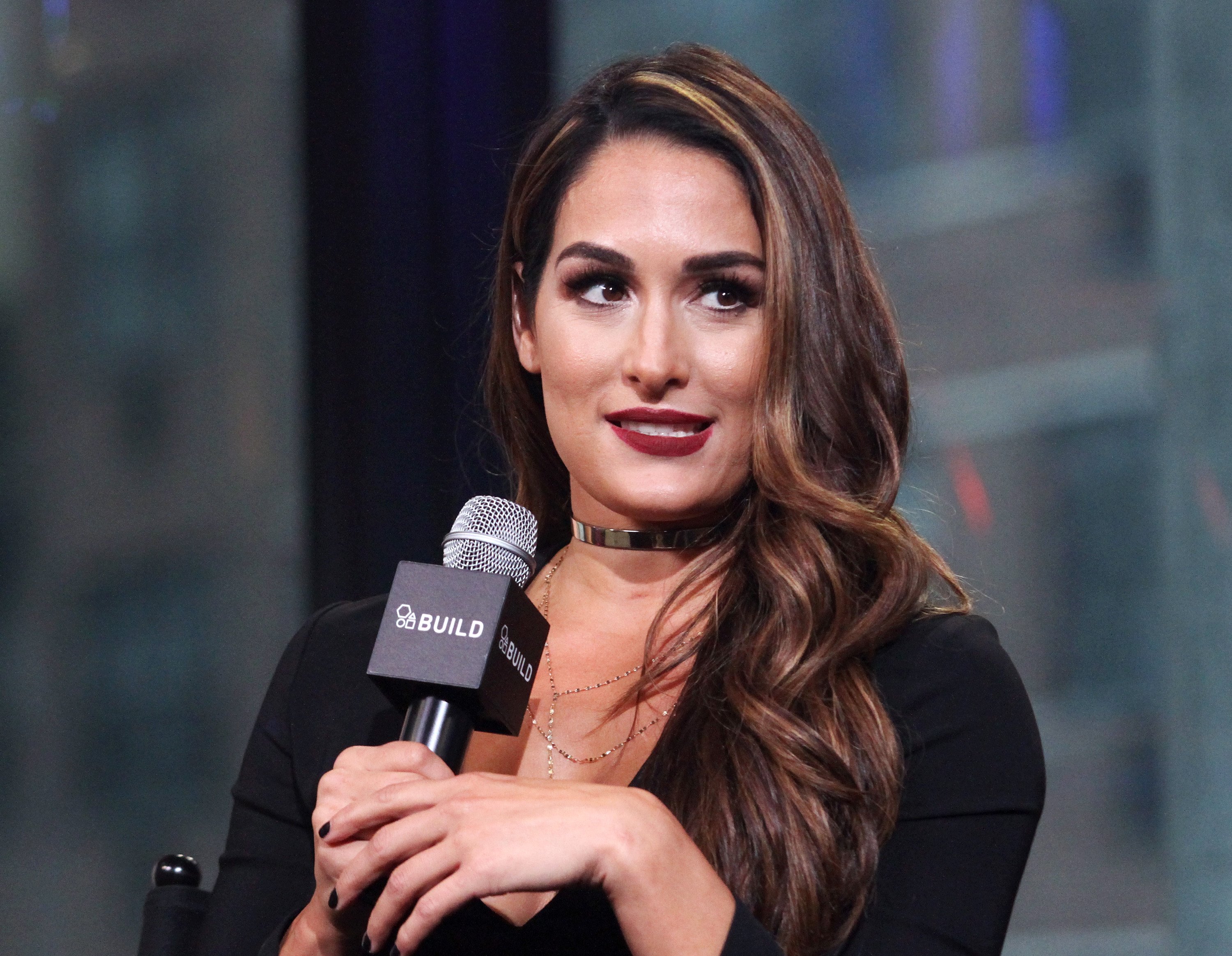 'Total Divas' star Nikki Bella dressed in black, holds a microphone while answering interview questions.