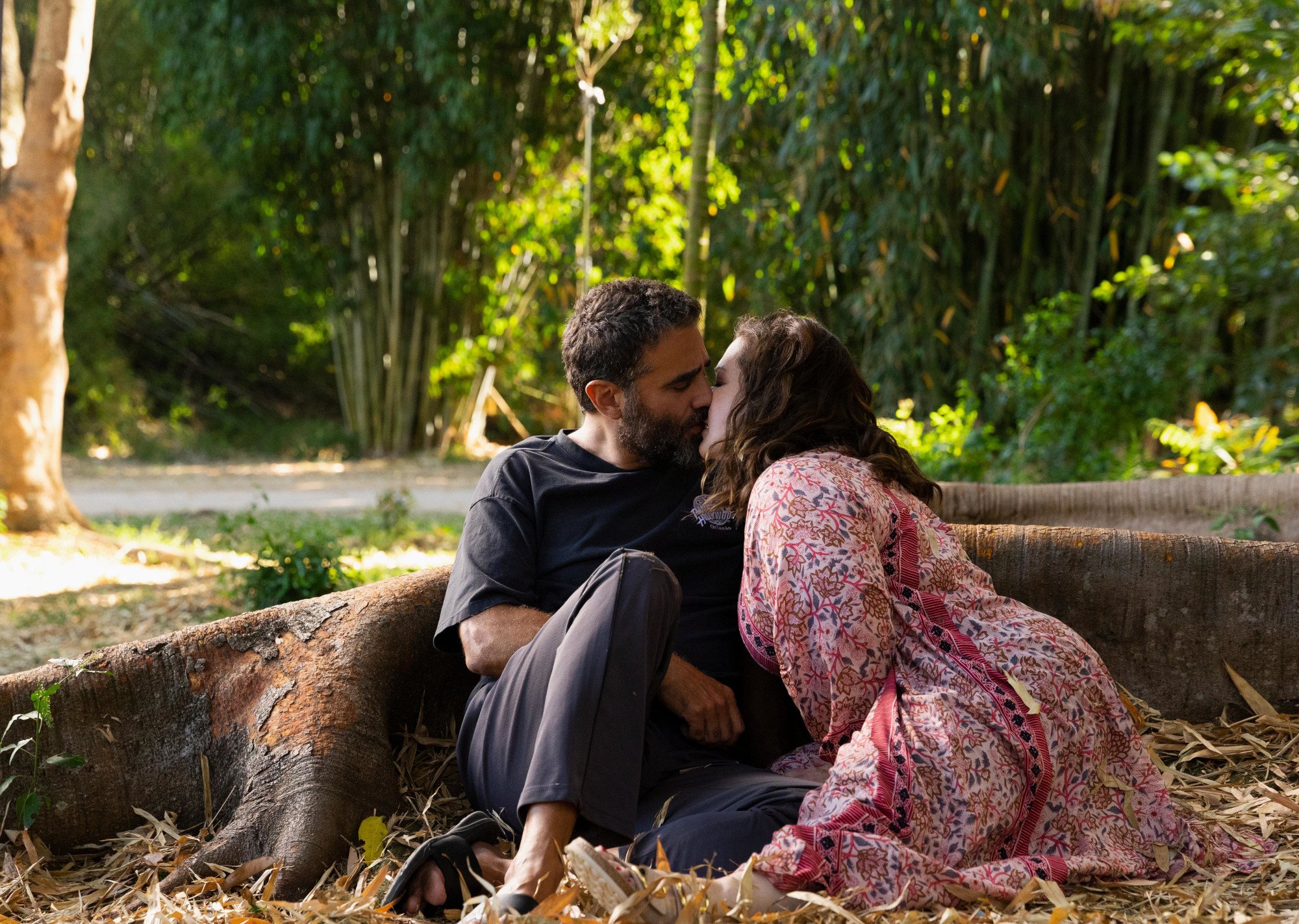 Bobby Cannavale as Tony and Melissa McCarthy as Frances in Hulu's 'Nine Perfect Strangers' Episode 6. They're kissing beneath a tree. Frances wears a pink dress and Tony wears dark pants and a black T-shirt.