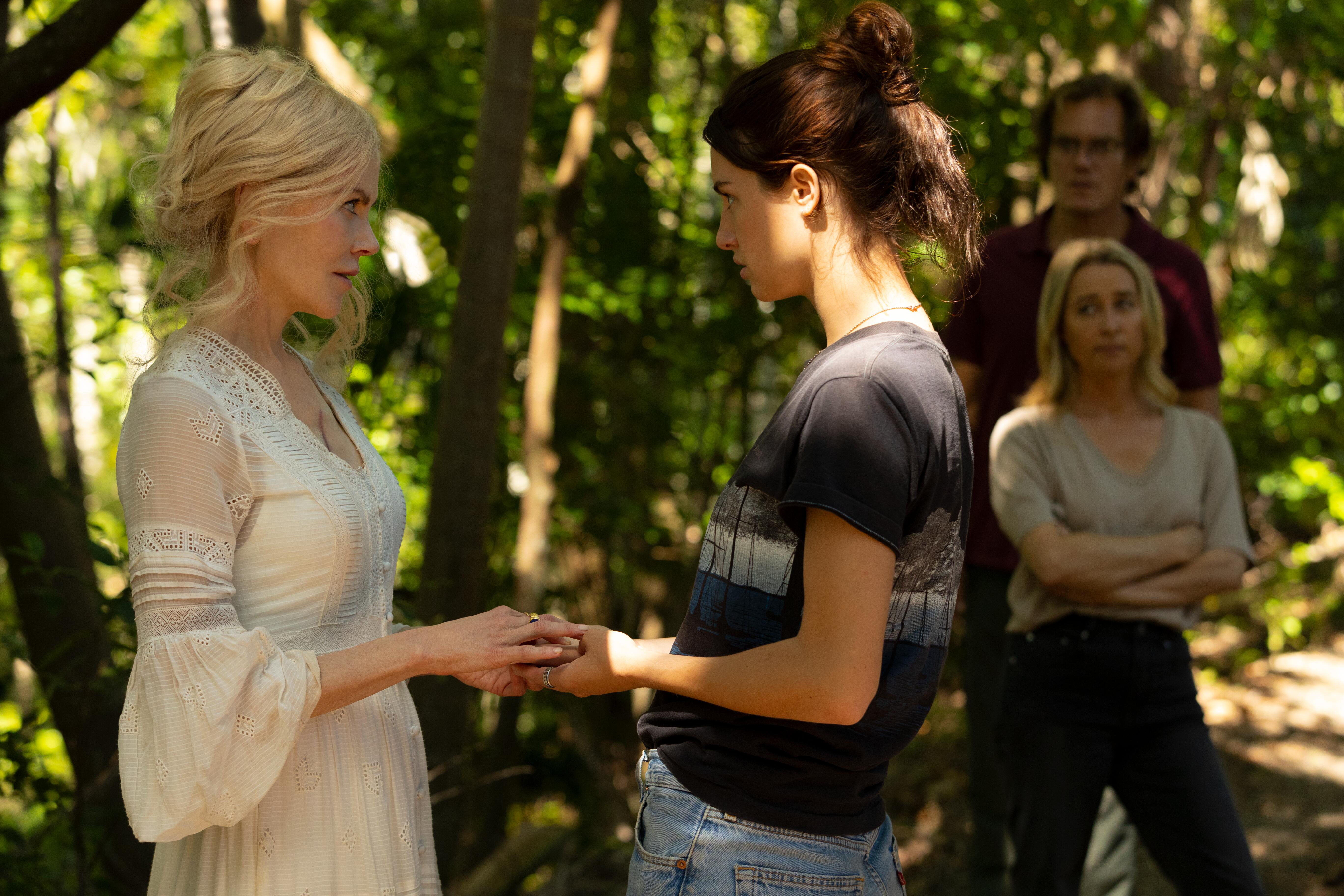 Masha and Zoe stand in the woods holding hands and looking at each other in 'Nine Perfect Strangers.' Napoleon and Heather watch them from the background. 