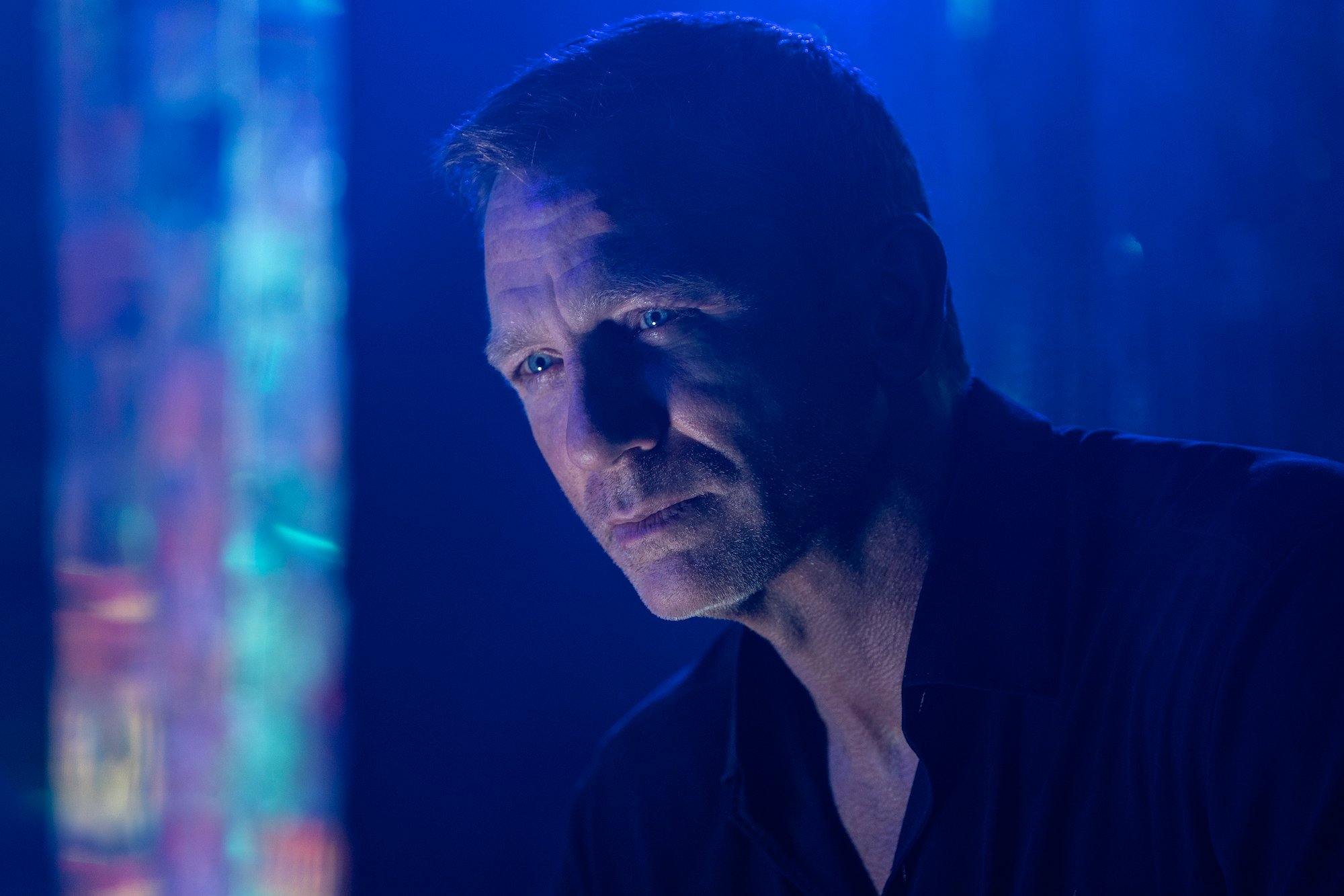 No Time to Die: Daniel Craig looks off screen with blue lights behind him.