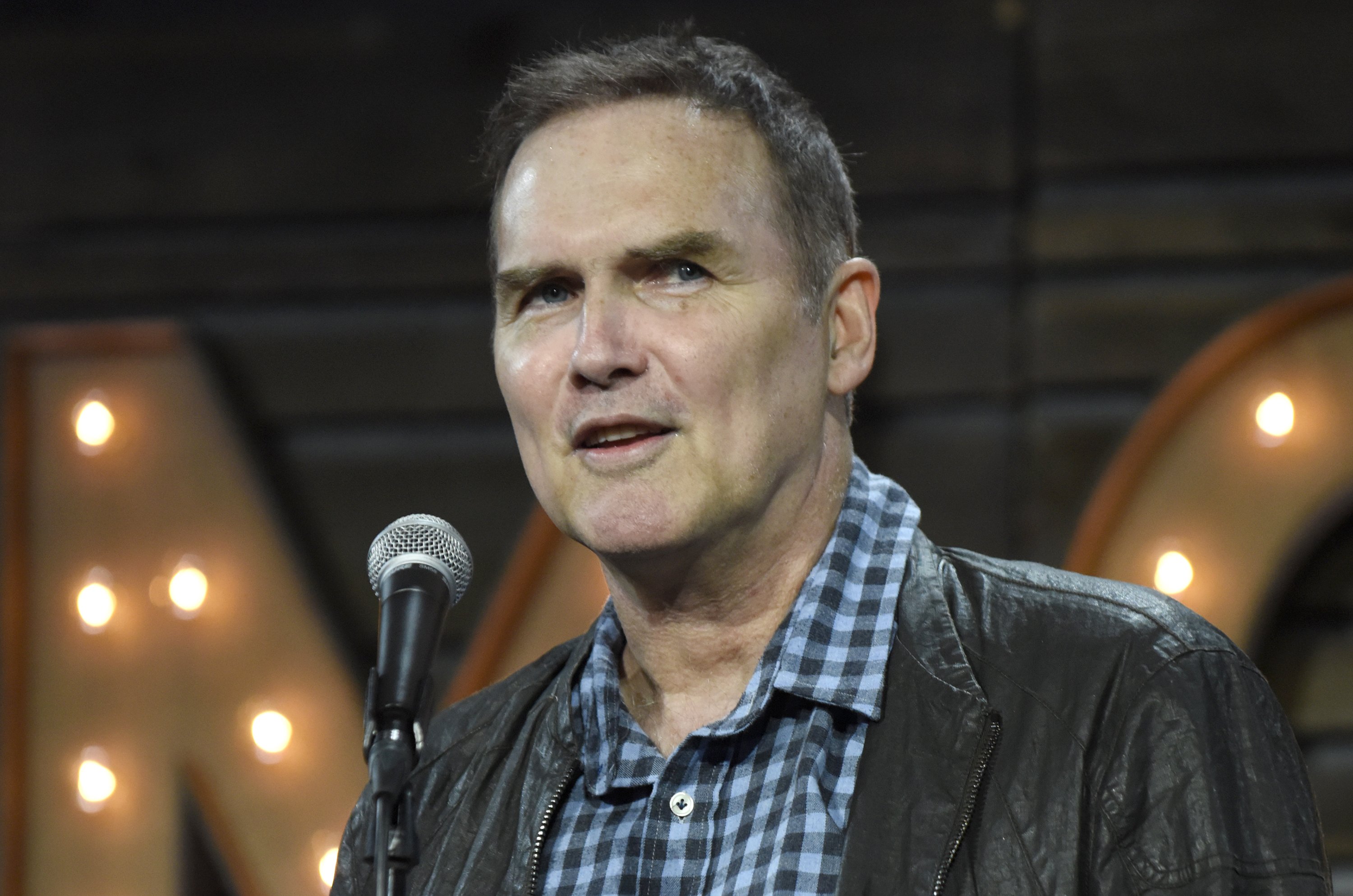 Norm Macdonald looking away from the camera next to a microphone.