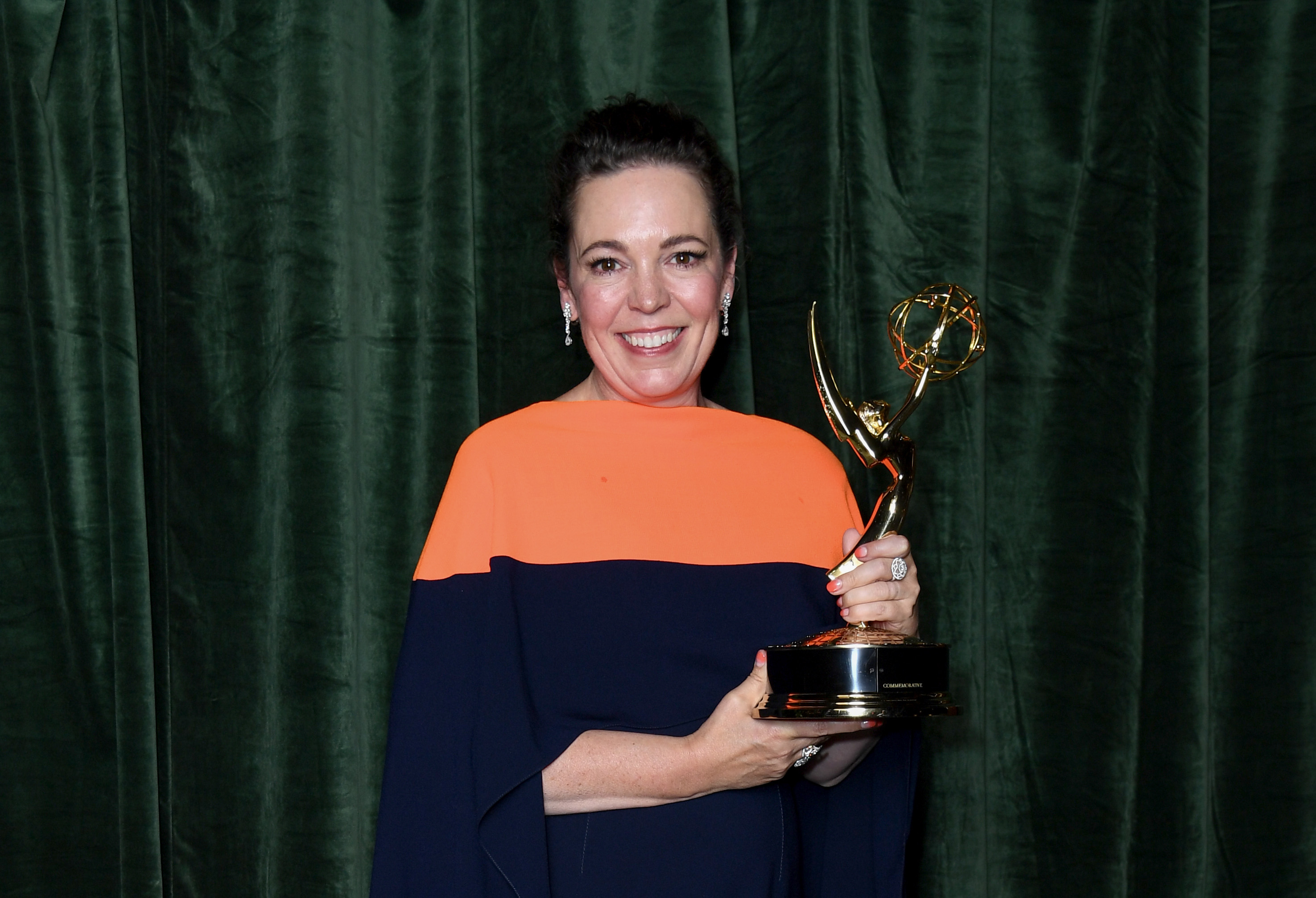 Olivia Colman holds her Emmy in 2021 for Netflix's 'The Crown.' She wears a blue and orange dress.