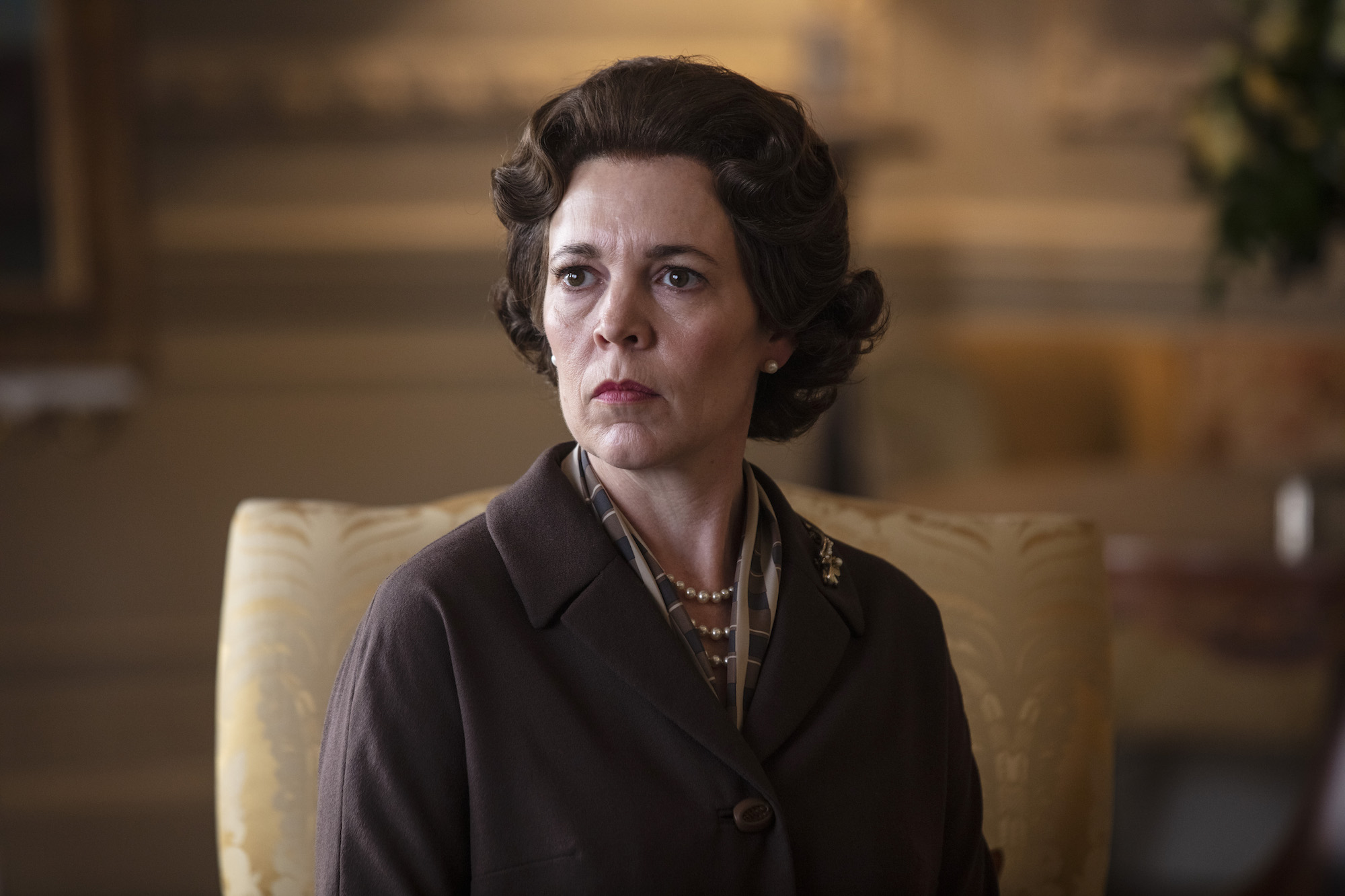 2021 Emmy nominee Olivia Colman sitting in a gold colored chair in 'The Crown.'