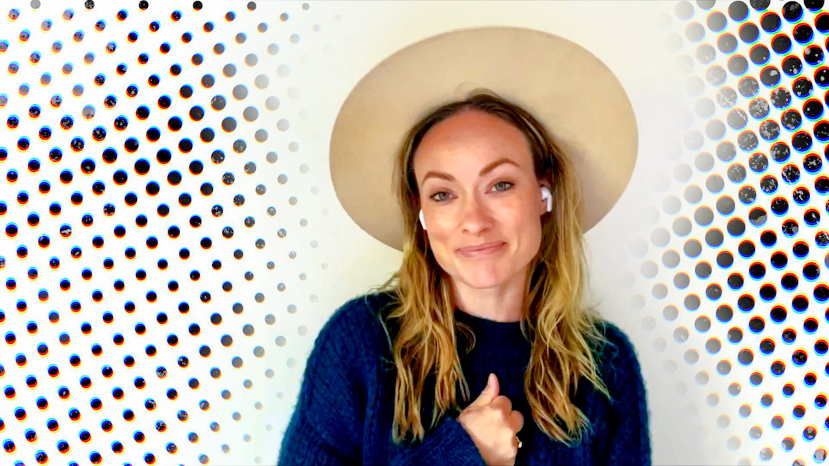 Olivia Wilde smiles while wearing a hat and earbuds.