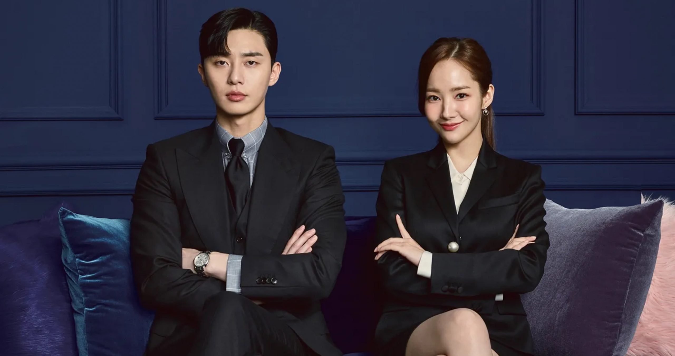Actors Park Seo-Joon and Park Min-Young in 'What's Wrong with Secretary Kim?' K-drama sitting on couch in work attire
