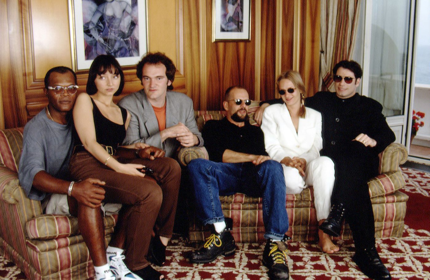 Part of the cast and crew of 'Pulp Fiction' sits on a couch in a colorful room.