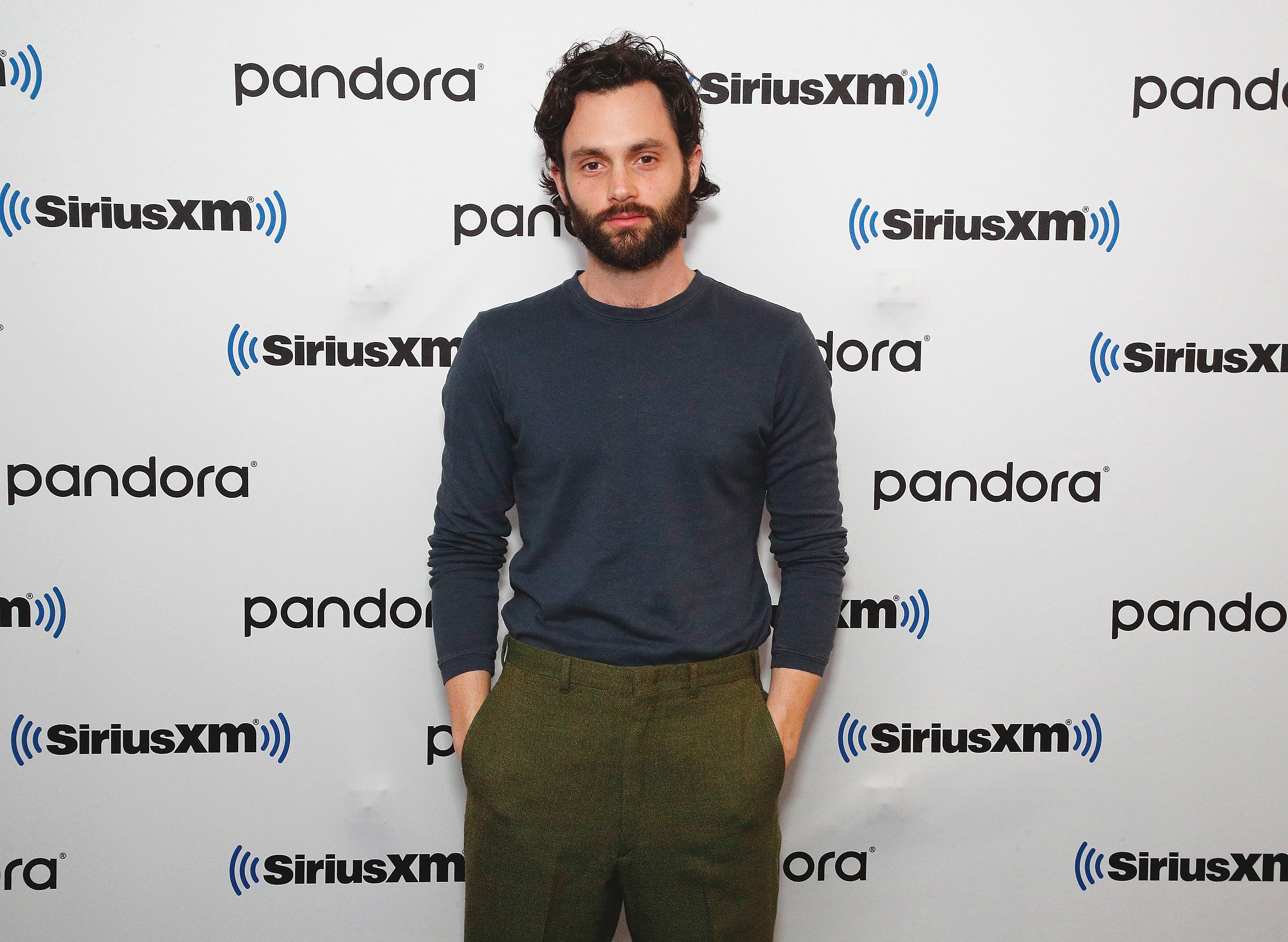 Penn Badgley in a blue shirt and green pants.