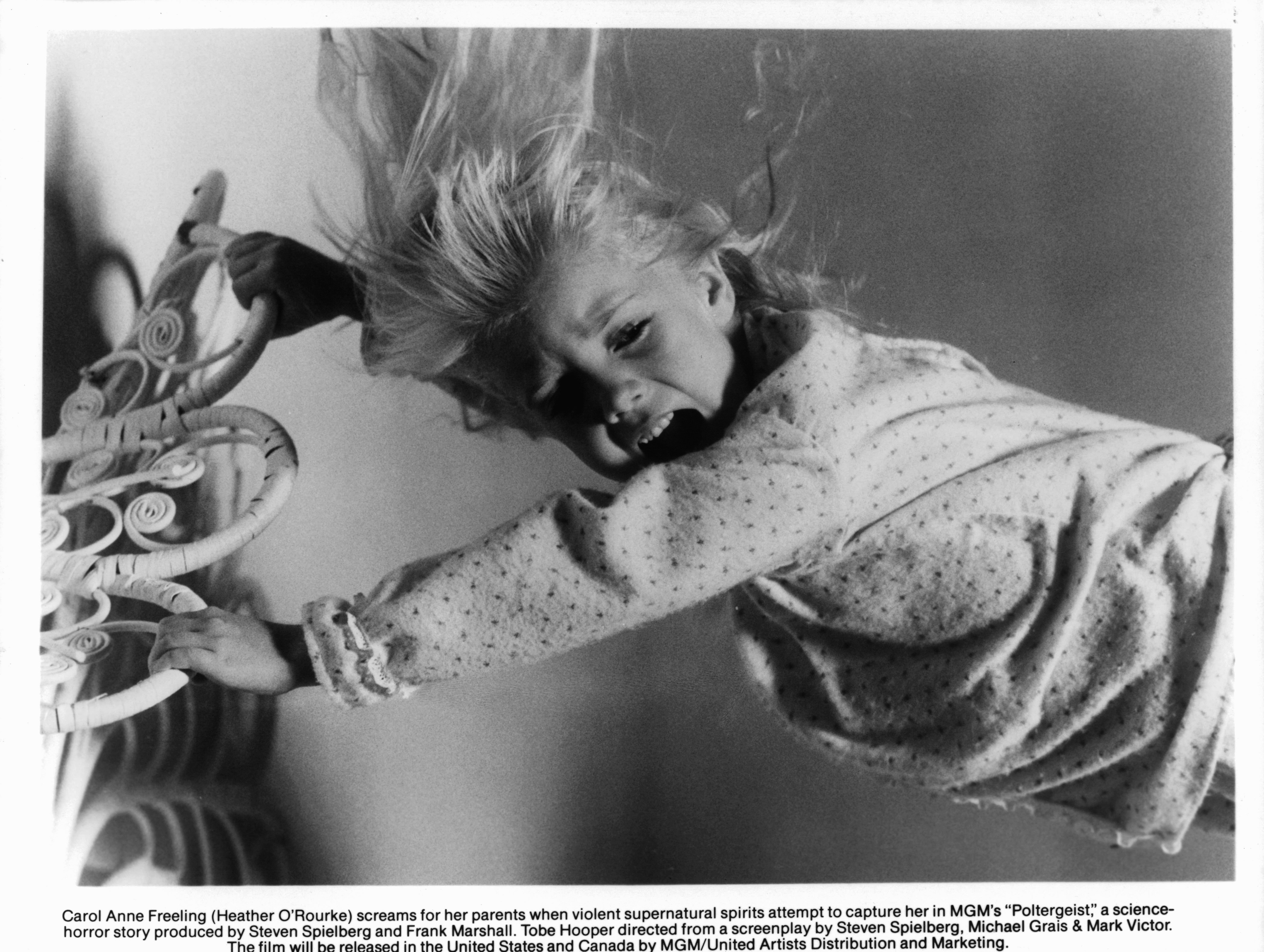 A young Heather O'Rourke grips the bedframe in Steven Spielberg's Poltergeist horror movie, one of the many horror movies based on a true story