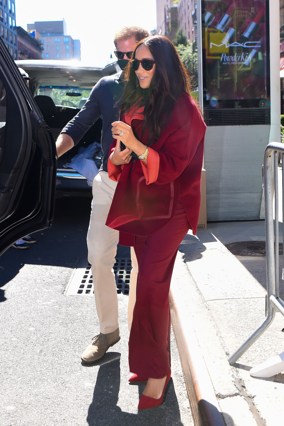 Prince Harry wears a button-down shirt and khaki pants as he walks next to Meghan Markle in a red pantsuit