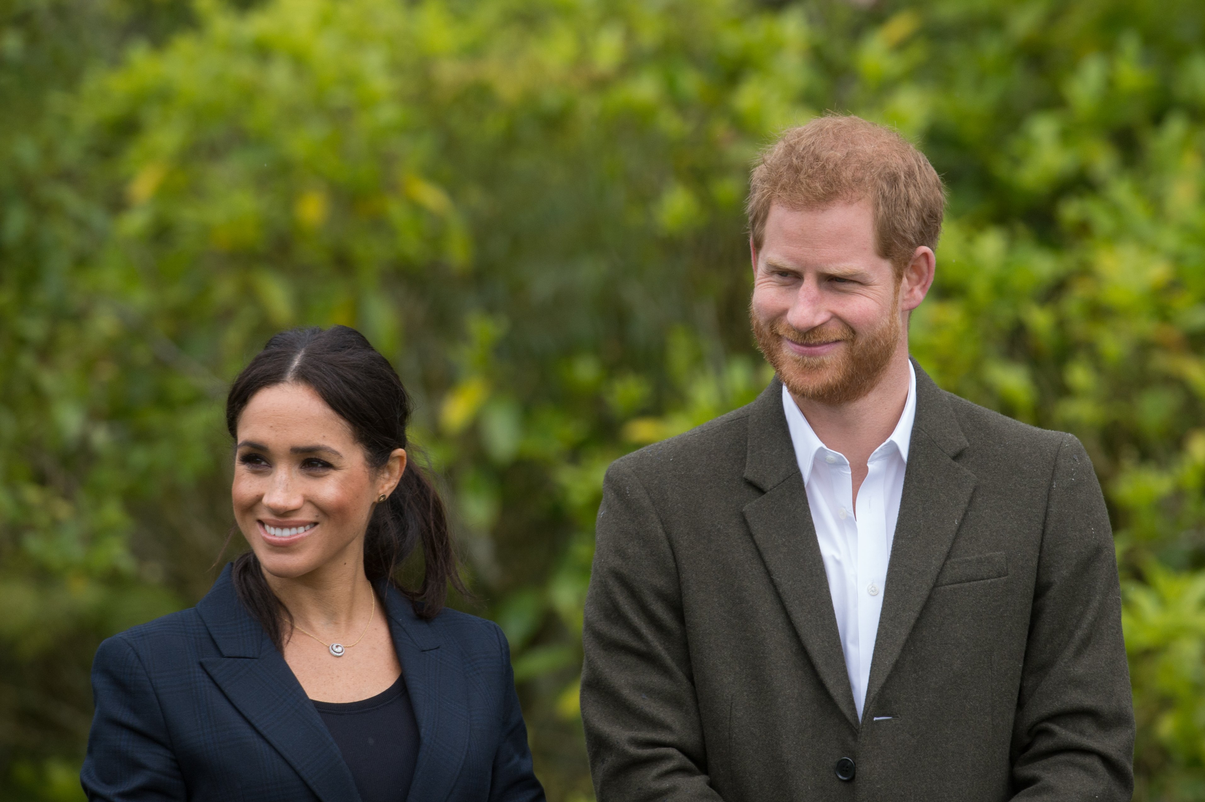 Meghan Markle and Prince Harry smiling in front of greenery