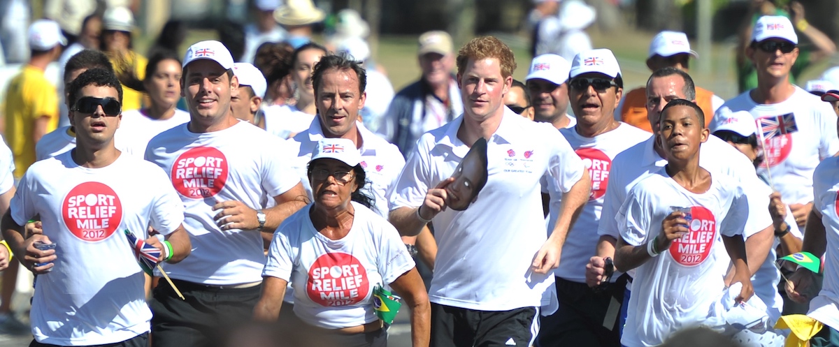 Prince Harry runs while holding a mask of Prince William