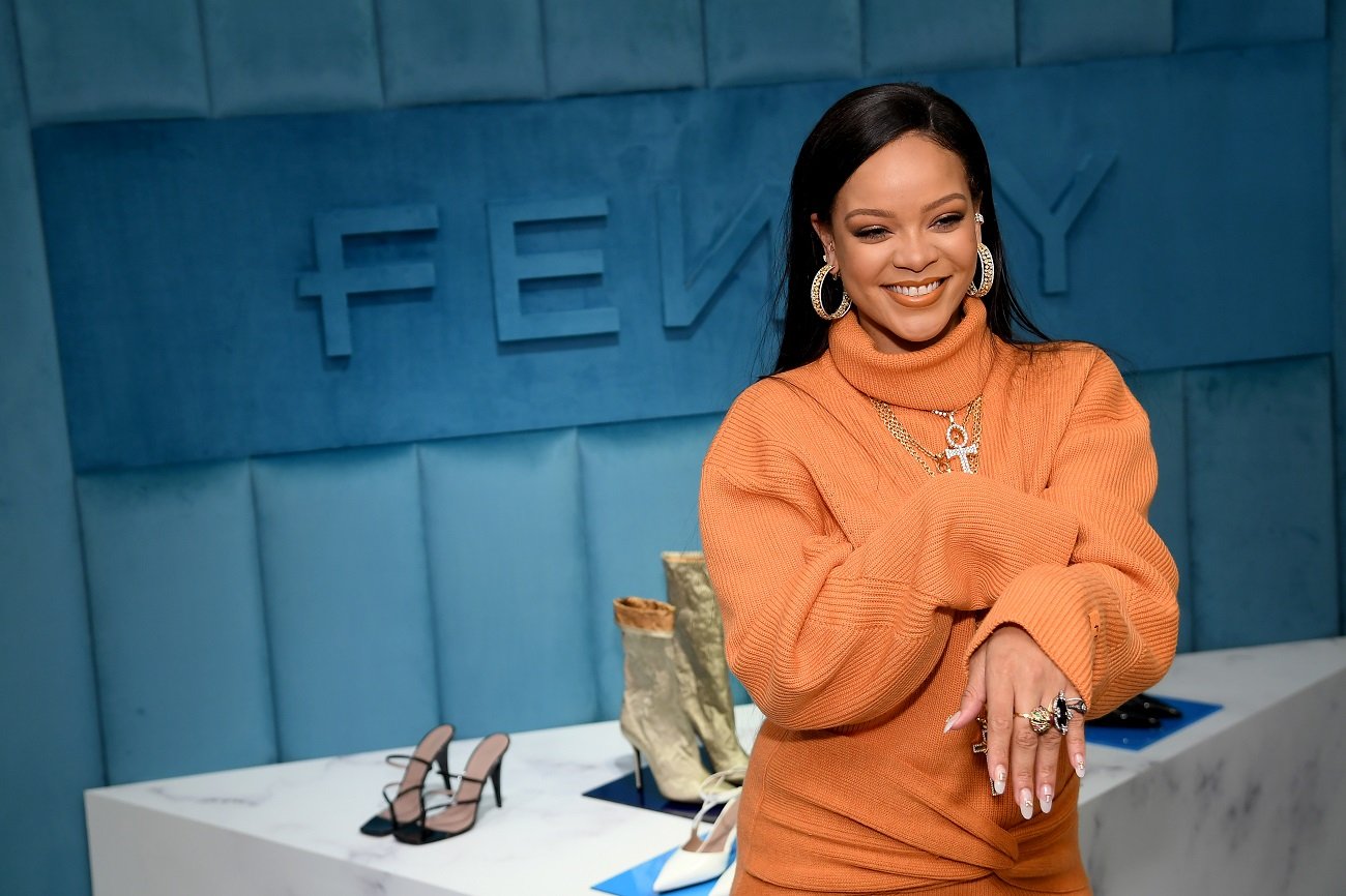 Rihanna, who recently achieved billionaire status, wears an orange sweater and shows off her rings.