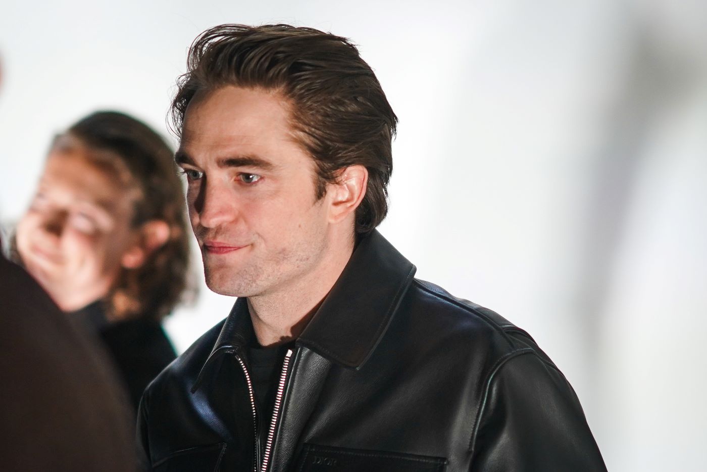 Robert Pattinson in a black leather jacket and black shirt against a white background.