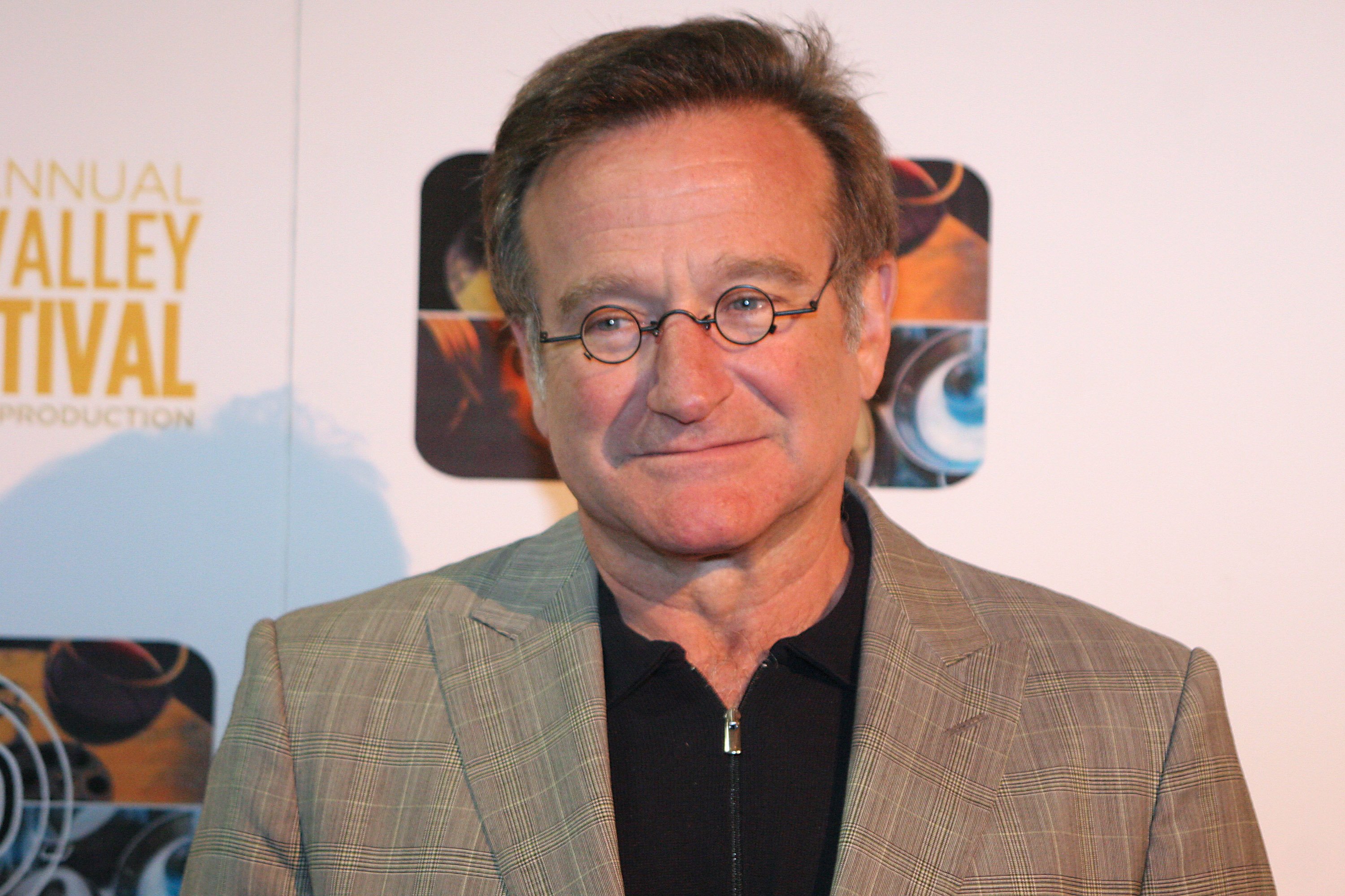 Robin Williams in black shirt and grey jacket from chest-up.
