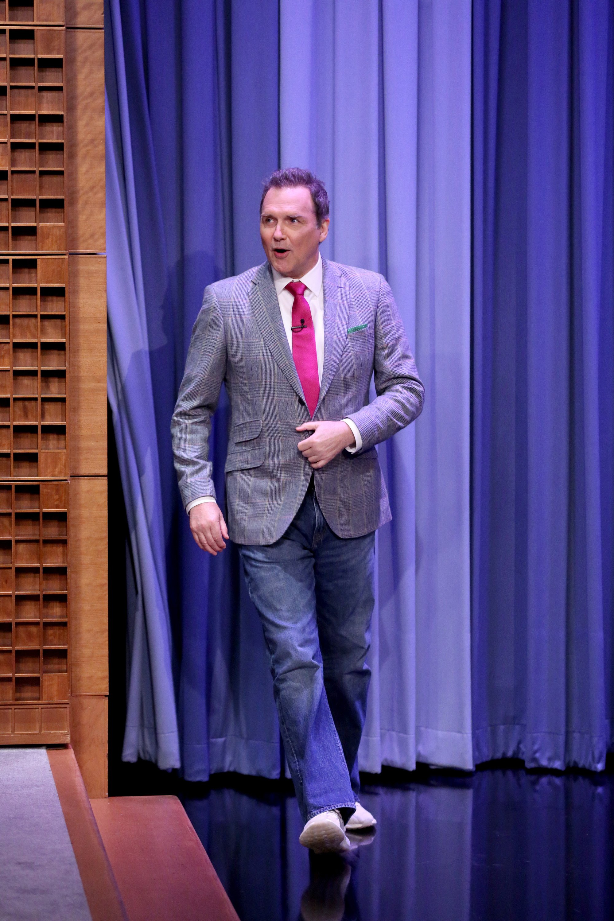 'SNL' alum and actor Norm Macdonald walking on stage in a blazer and jeans.