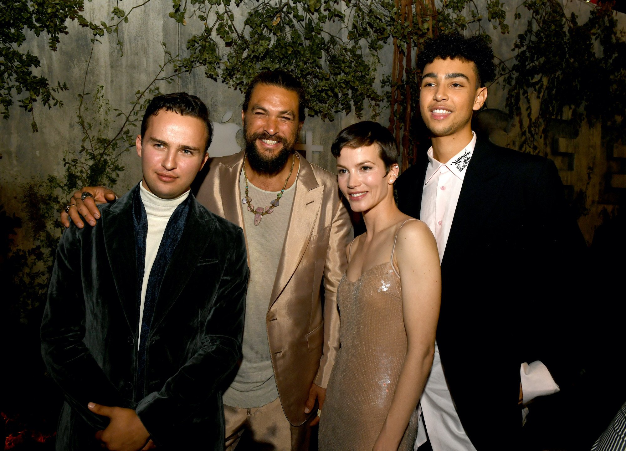 Cast members of 'See' smiling in front of a movie poster