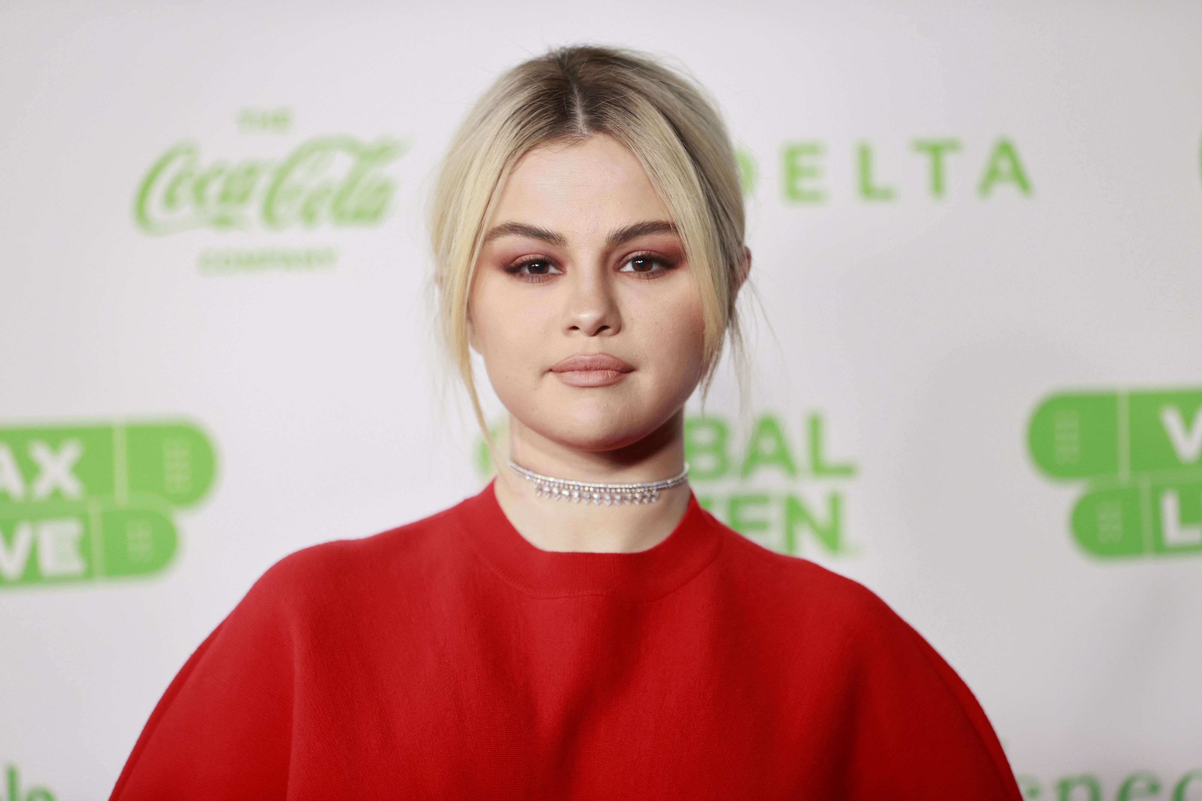 Selena Gomez with blonde hair, wearing a red sweater.