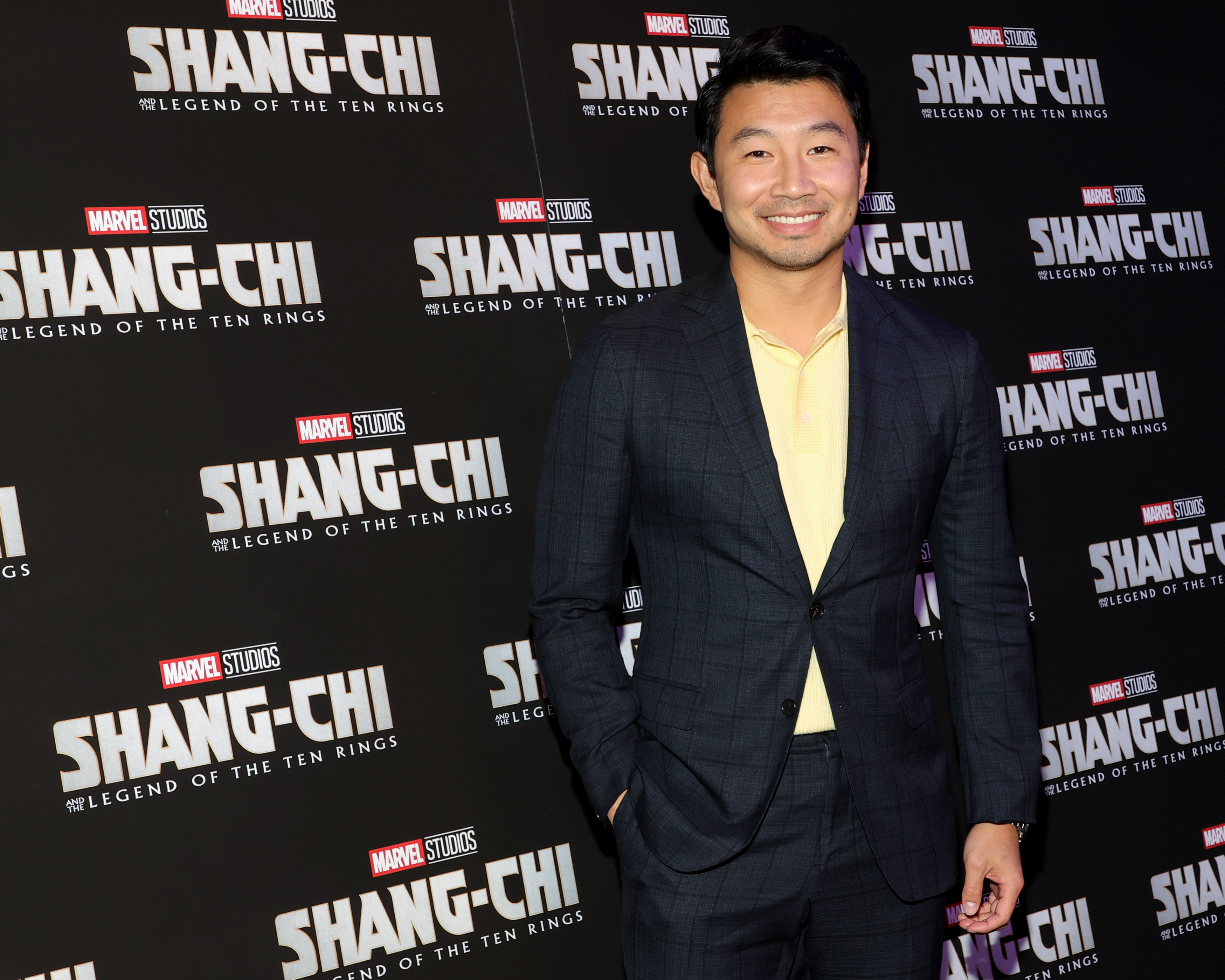 'Shang-Chi' star Simu Liu wears a black suit over a yellow shirt.