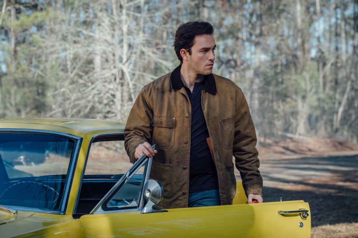 'Stargirl' actor Cameron Gellman, as his character Rick Tyler, steps out of a yellow car wearing a brown jacket over a dark blue shirt..