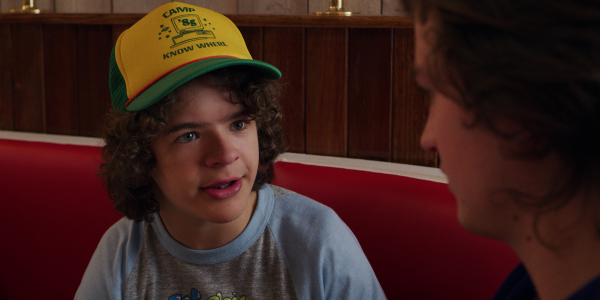Gaten Matarazzo as Dustin looks at the camera in a yellow and green hat in a production still from 'Stranger Things' Season 3.