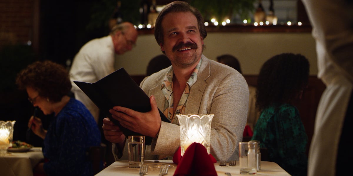 David Harbour as Chief Jim Harbour holding a menu at a restaurant in a production still from 'Stranger Things' Season 3.