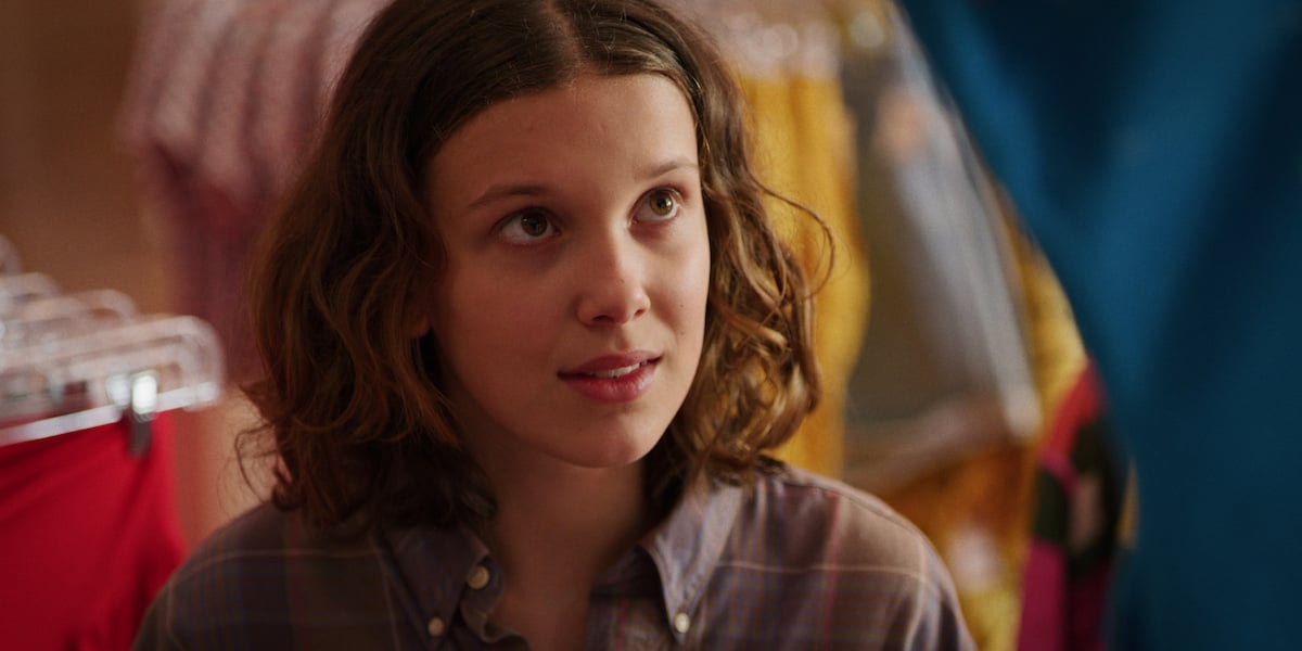 Eleven, played by Millie Bobby Brown, in a flannel shirt looking up in a production still from 'Stranger Things' Season 3.
