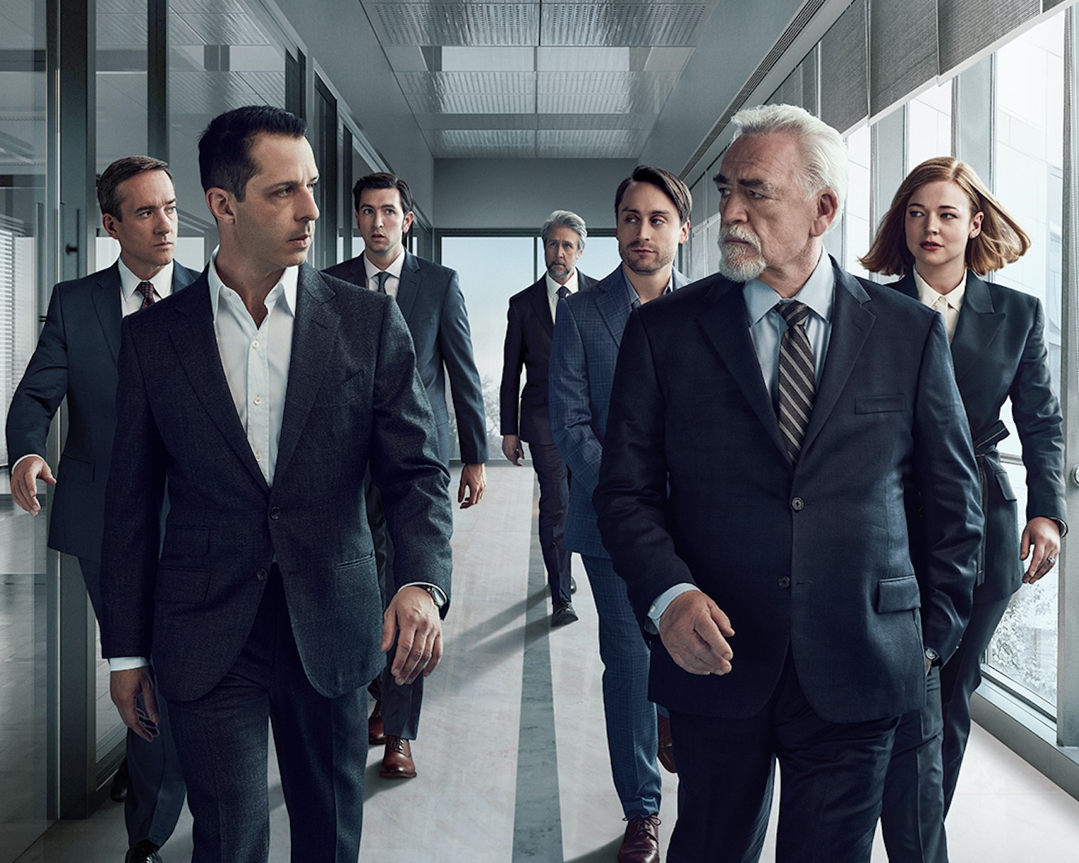 The cast of 'Succession' wears suits and walks down a hallway.