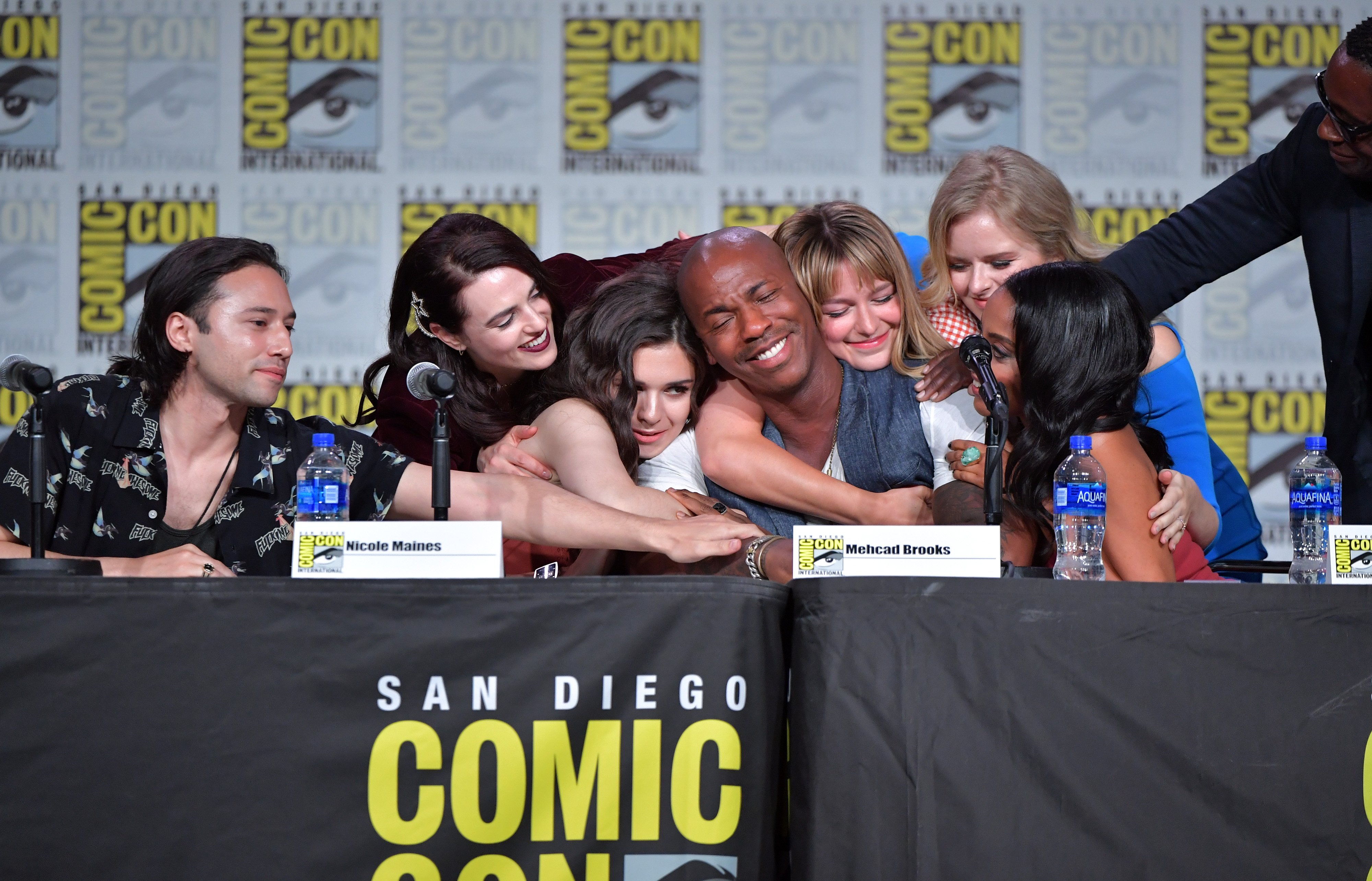 The 'Supergirl' series finale cast, Jesse Rath, Katie McGrath, Nicole Maines, Mechad Brooks, Melissa Benoist, Andrea Brooks, Azie Tesfai, and David Harewood, embrace onstage during a San Diego Comic-Con panel.