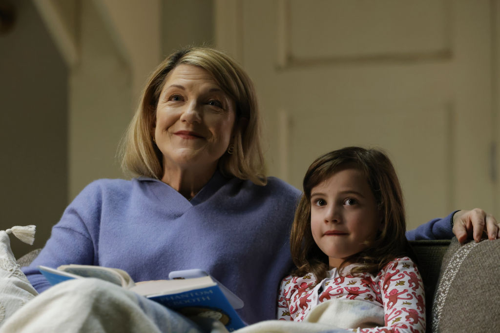 Victoria Clark as Mrs. French, Hazel and Ginger Mason as Agnes Keen sit on the couch together to read a book.