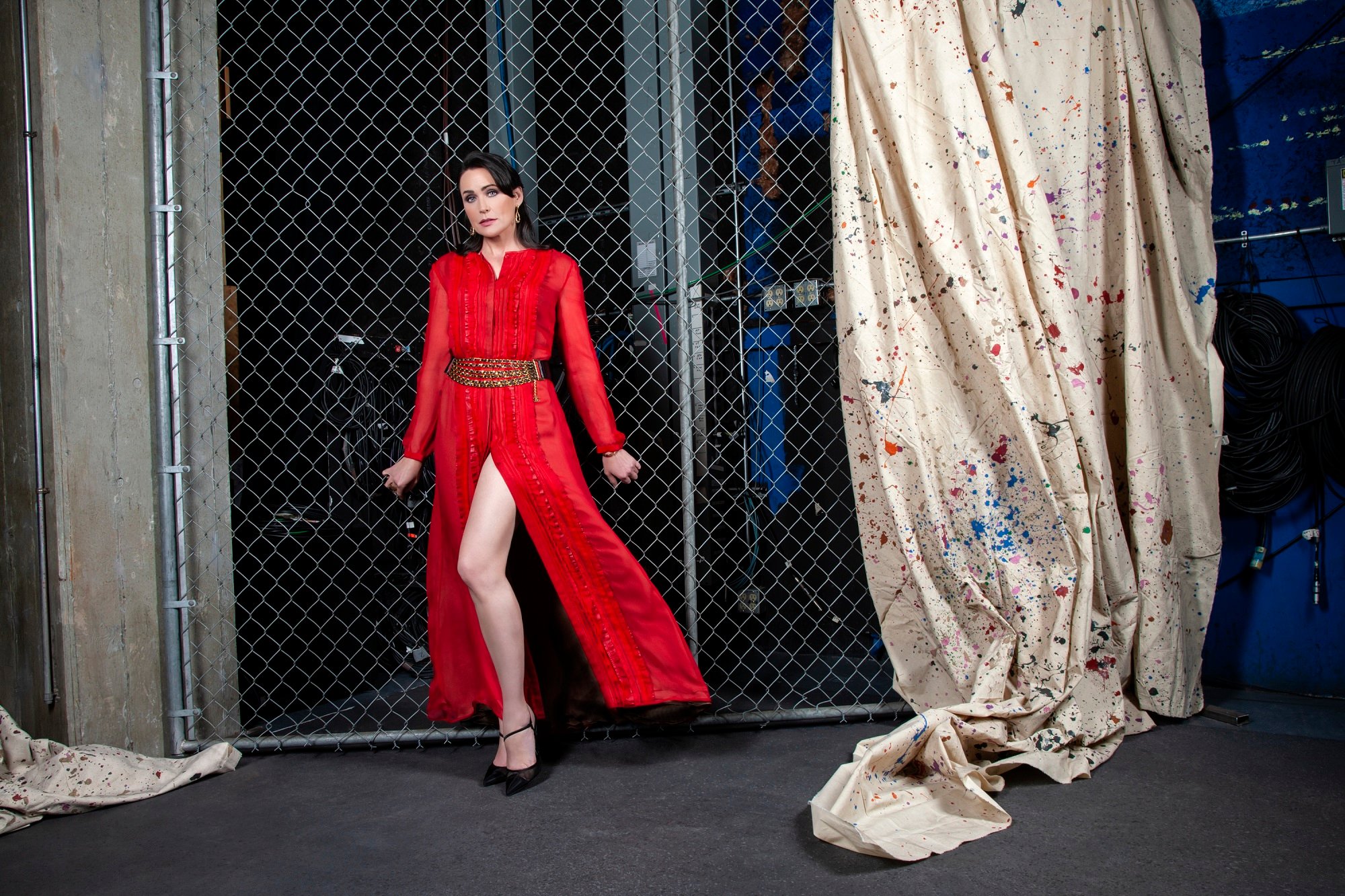 The Bold and the Beautiful spoilers focus on Rena Sofer's character of Quinn, pictured here in a red dress leaning up against a metal gate