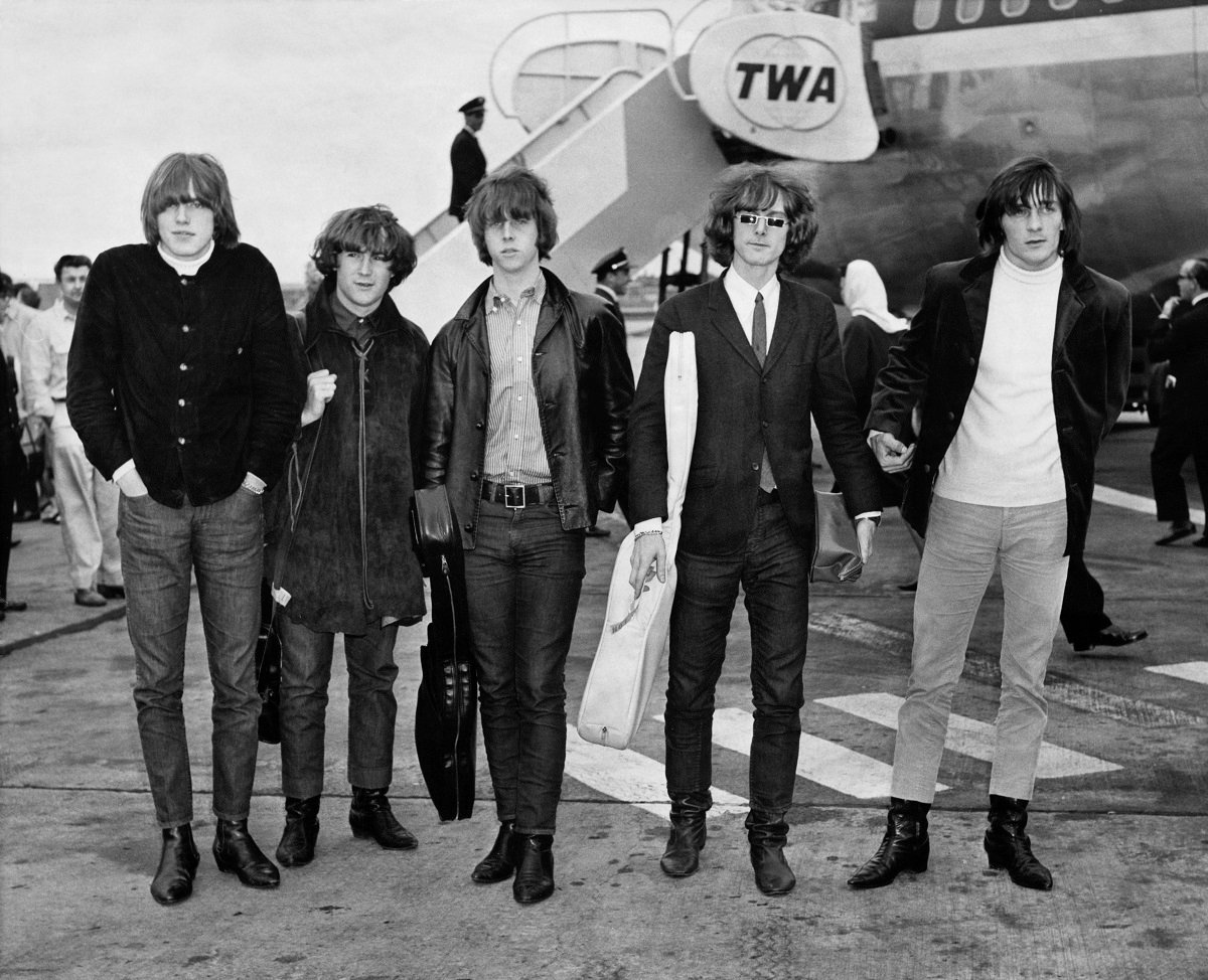 The Byrds on an airport tarmac in front of a plane in a black and white image. 