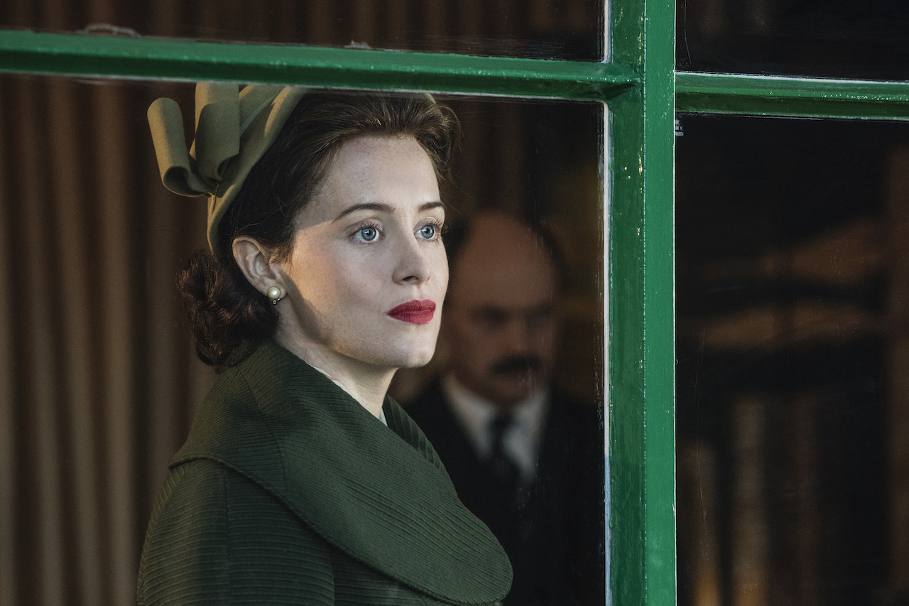 Claire Foy as Queen Elizabeth II on 'The Crown' wears a green dress and hat. She looks out a window.