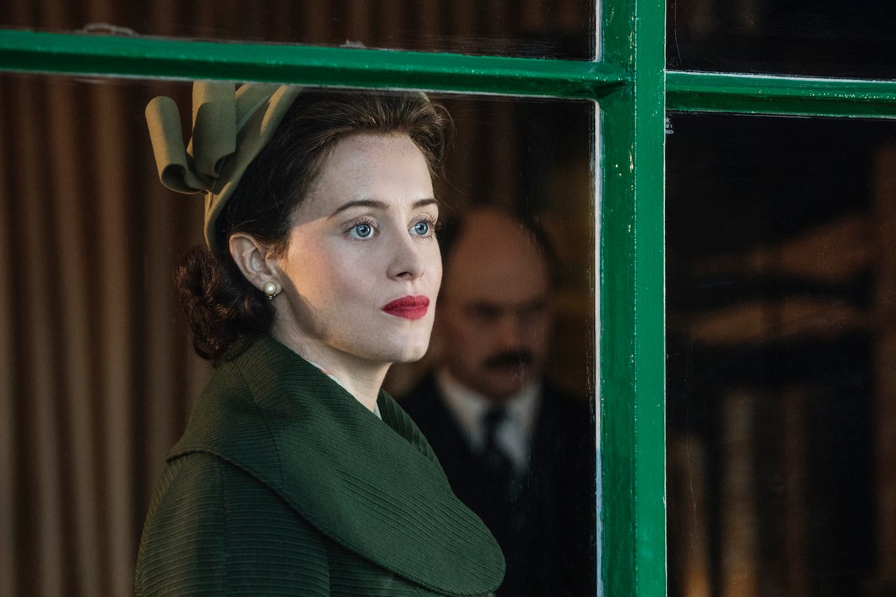 Claire Foy as Queen Elizabeth II on 'The Crown' wears a green dress and hat. She looks out a window.