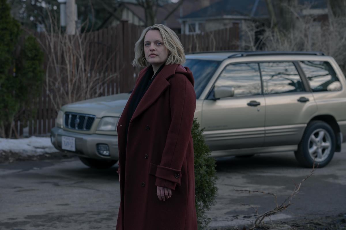 Elisabeth Moss as June in 'The Handmaid's Tale' Season 4 Episode 10, 'The Wilderness.' She stands in a driveway looking at a house that's offscreen. Moss is wearing a long red coat that's similar in color to the dress she had to wear as a Handmaid in Gilead. It's daytime in the winter.