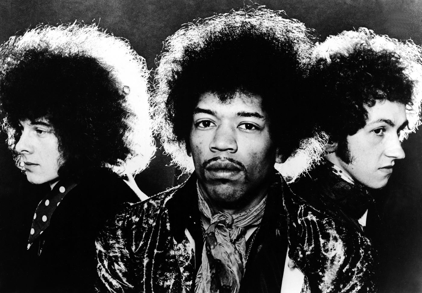 The Jimi Hendrix Experience with Noel Redding, Jimi Hendrix, and Mitch Mitchell in front of a black background.