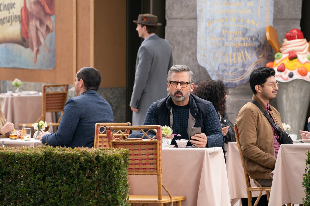 Mitch Kessler sits at a table outside a gelato shop in 'The Morning Show' Season 2. He is holding a spoonful of gelato and has a confused expression on his face. 