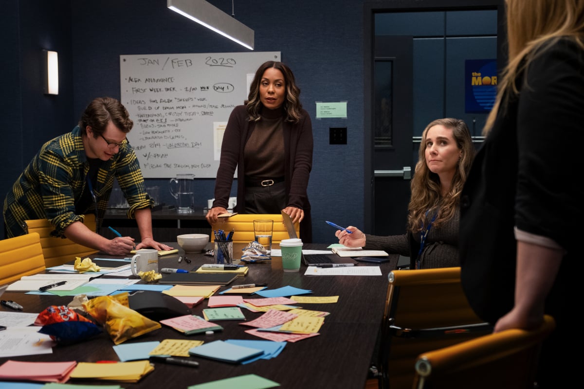 Mia, Rena, and two of their coworkers brainstorm ideas in 'The Mornin Show' Season 2. They are sitting and standing around a table covered in sticky notes with a whiteboard in the background.