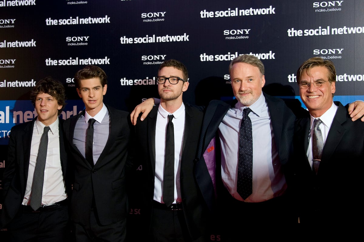 Jesse Eisenberg, Andrew Garfield, Justin Timberlake, David Fincher, and Aaron Sorkin attend the premiere of 'The Social Network' in Paris. The men stand side-by-side in black suits and ties with their arms around each other. They stand in front of a backdrop that says 'The Social Network' and 'SONY' in white lettering. Fincher directed the three actors in the Oscar-winning movie. And Fincher is known for making actors do many takes, which Garfield found to be exhausting, but gratifying.
