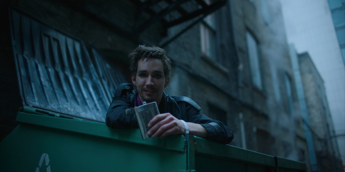 Robert Sheehan as Klaus Hargreeves leaning over the edge of a dumpster with a flask in his hand in a scene from 'The Umbrella Academy' Season 1.