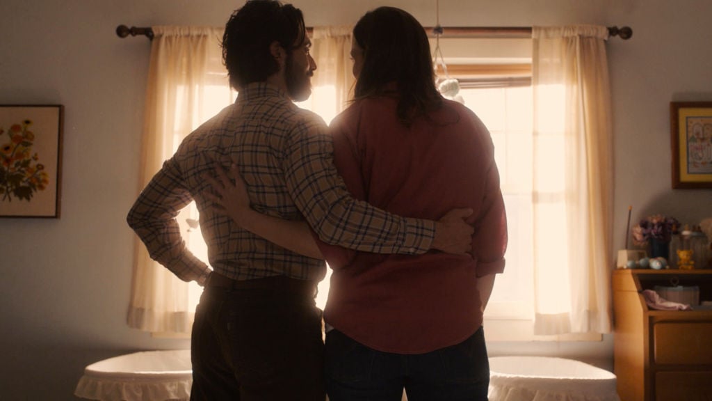 Milo Ventimiglia as Jack, Mandy Moore as Rebecca Pearson stand side-by-side with their back to the camera with their arms across each other's backs.