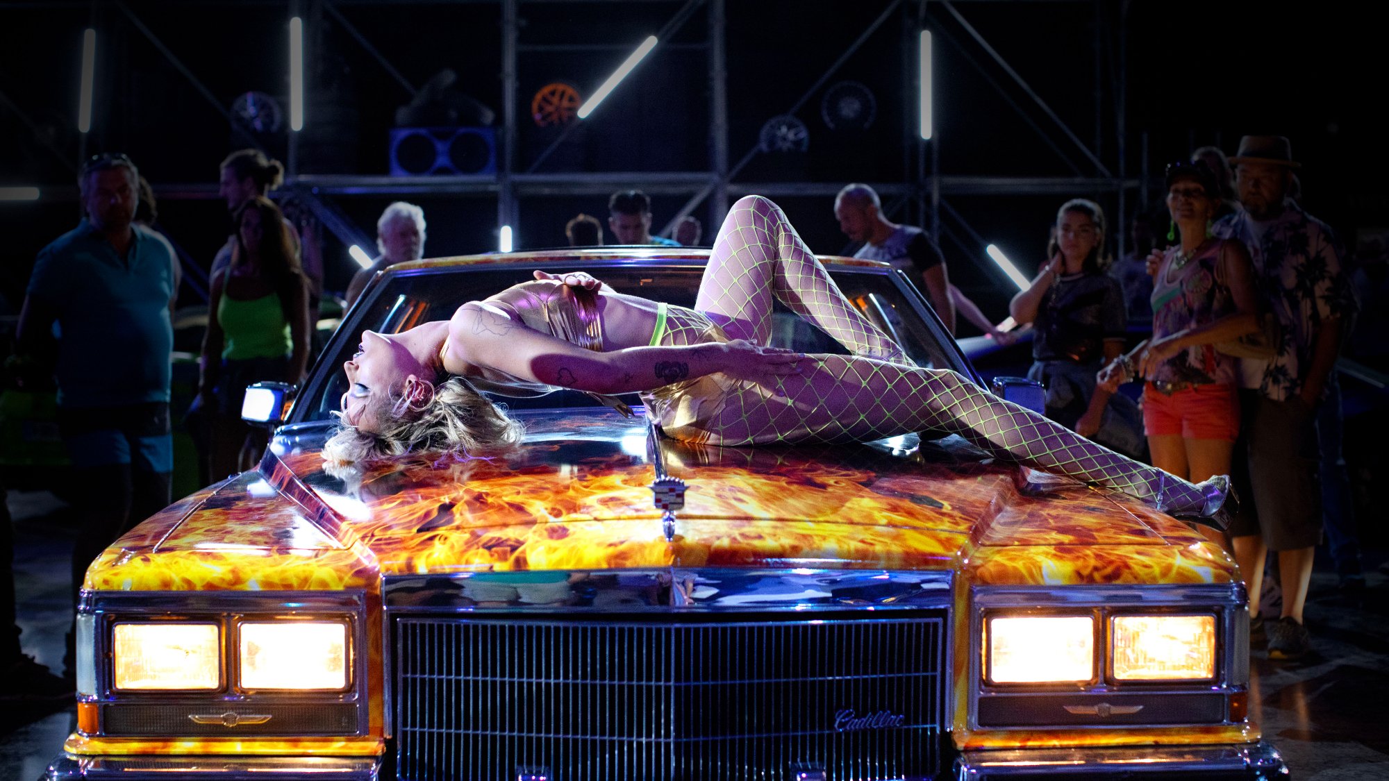 'Titane' Agathe Rousselle as Alexia laying on her back on the hood of a car with painted flames on it