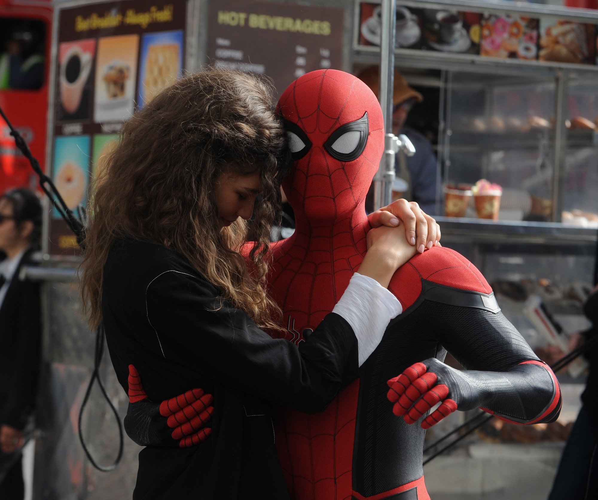 Tom Holland dressed as Spider-Man holding Zendaya as MJ. He's wearing the Spider-Man suit and she's wearing a black shirt and leaning her head against his.